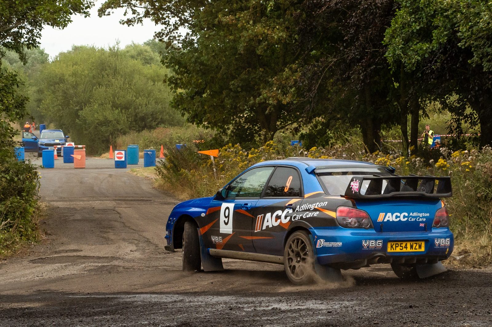 Blue Subaru Impreza rally car numbered 9, branded ACC Adlington Car Care, on a gravel stage